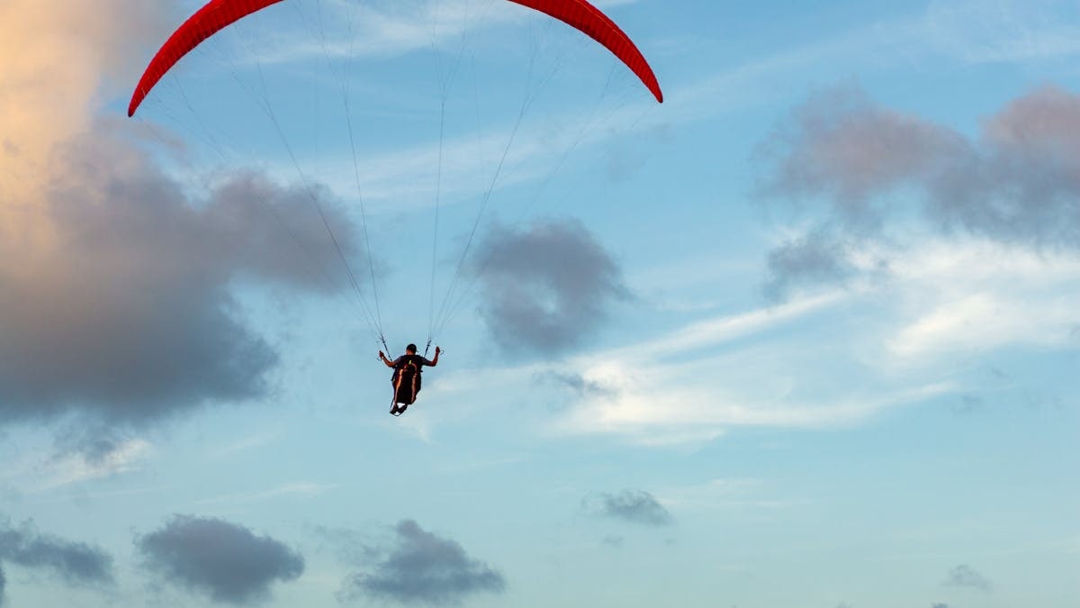 A paraglider soaring through the clouds with a vibrant red parachute, set against a dramatic Brazilian sky.