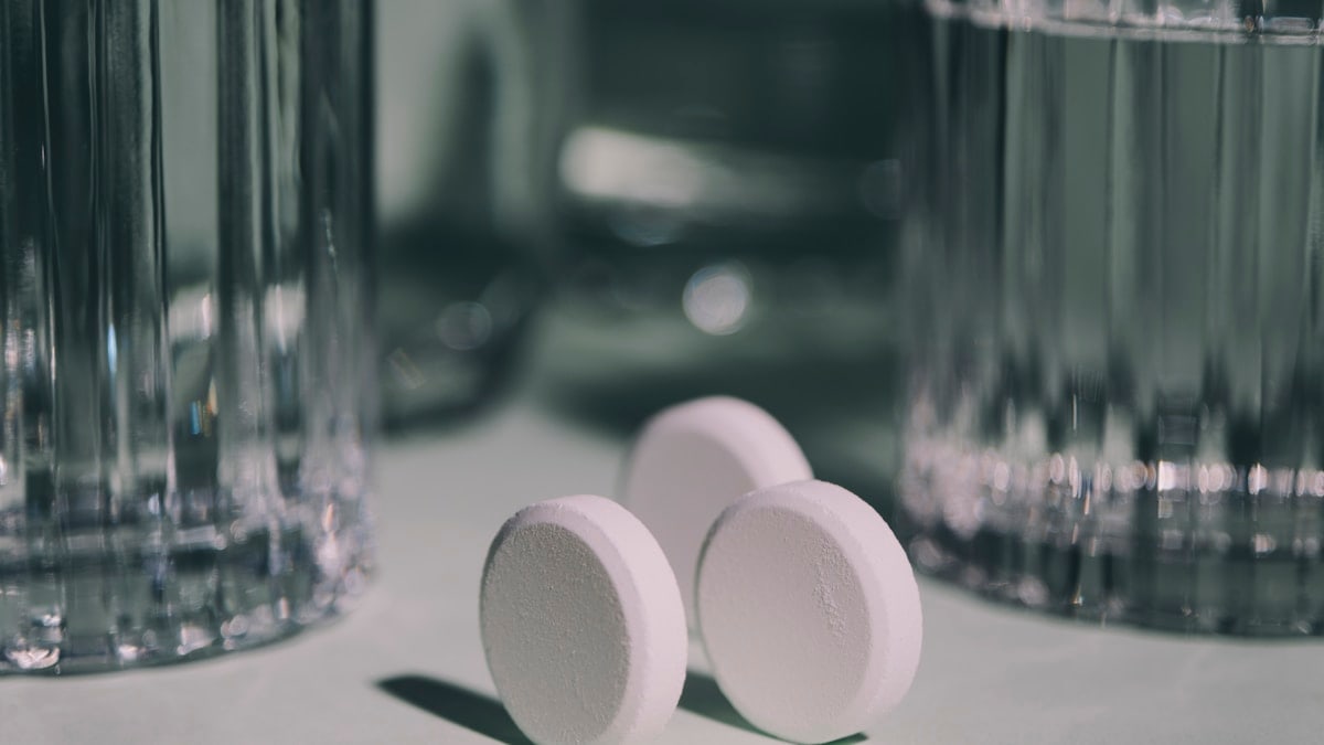 Three pills sitting on top of a table next to a glass of water